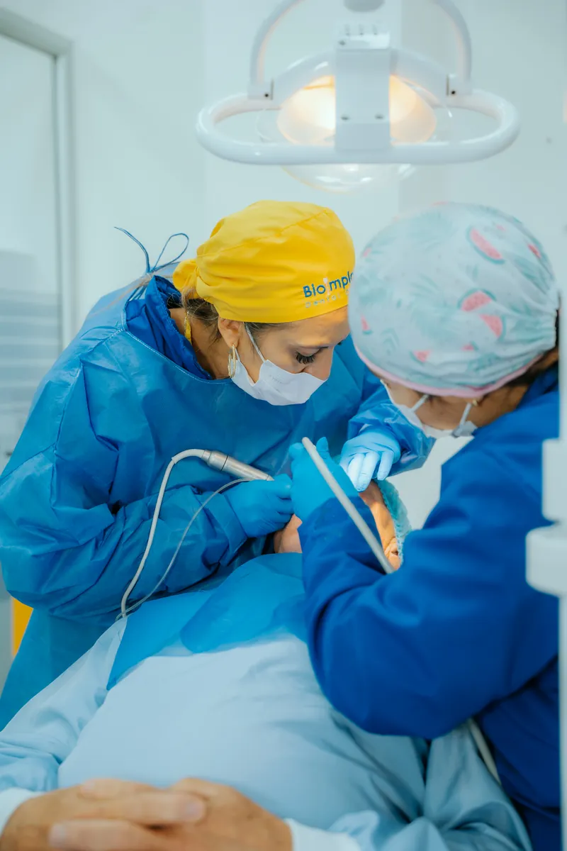 La odontóloga de Bioimplant, con gorro amarillo, trabaja en la boca de un paciente junto a su asistente