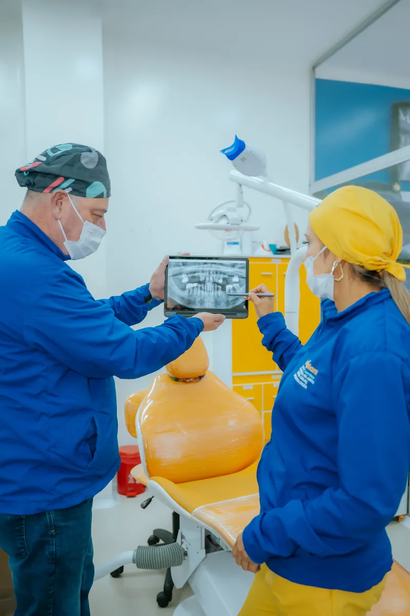 El odontólogo muestra una radiografía panorámica en una tableta junto al sillón amarillo